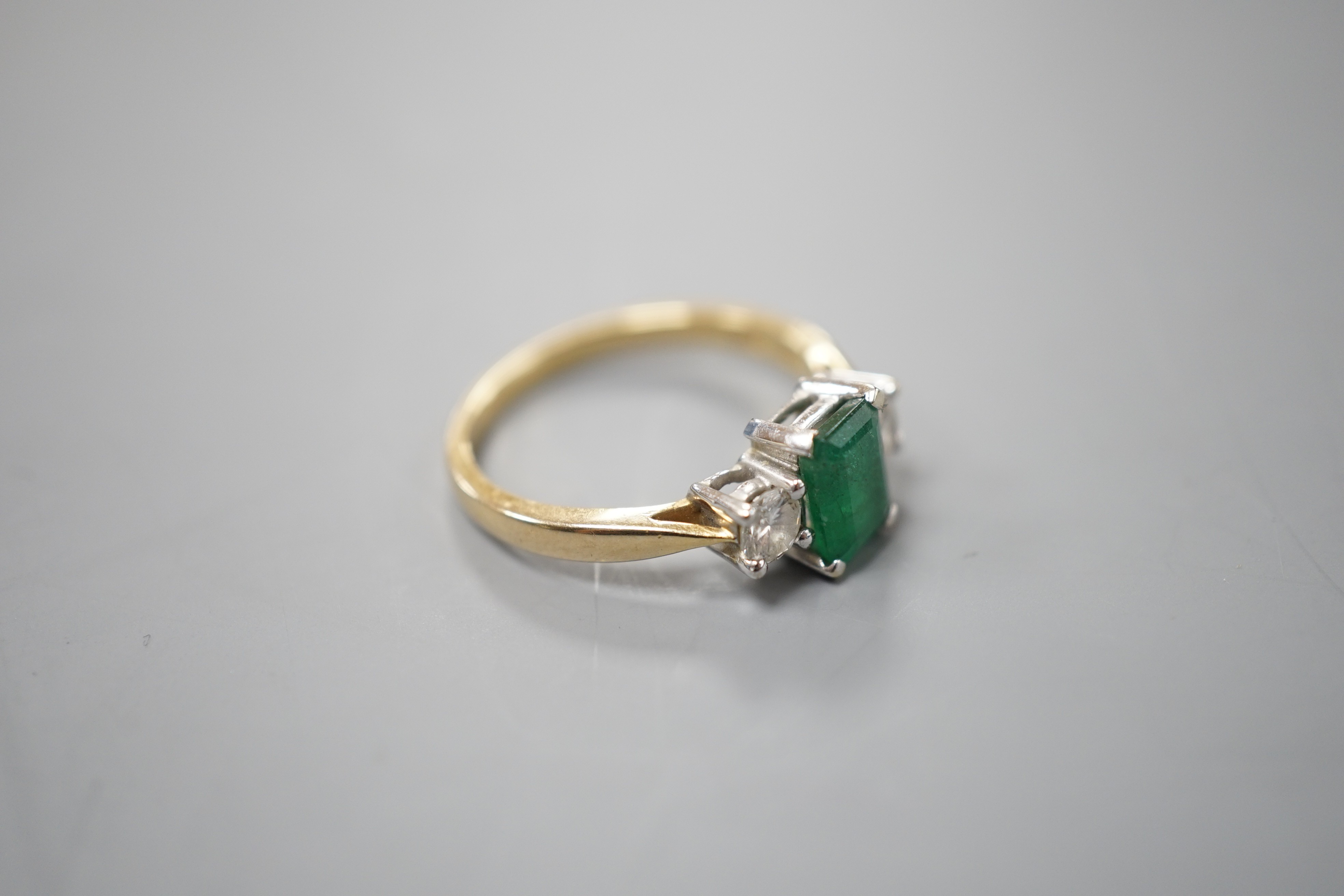 A modern 18ct gold, emerald and diamond set three stone ring, size N, gross weight 3.5 grams.